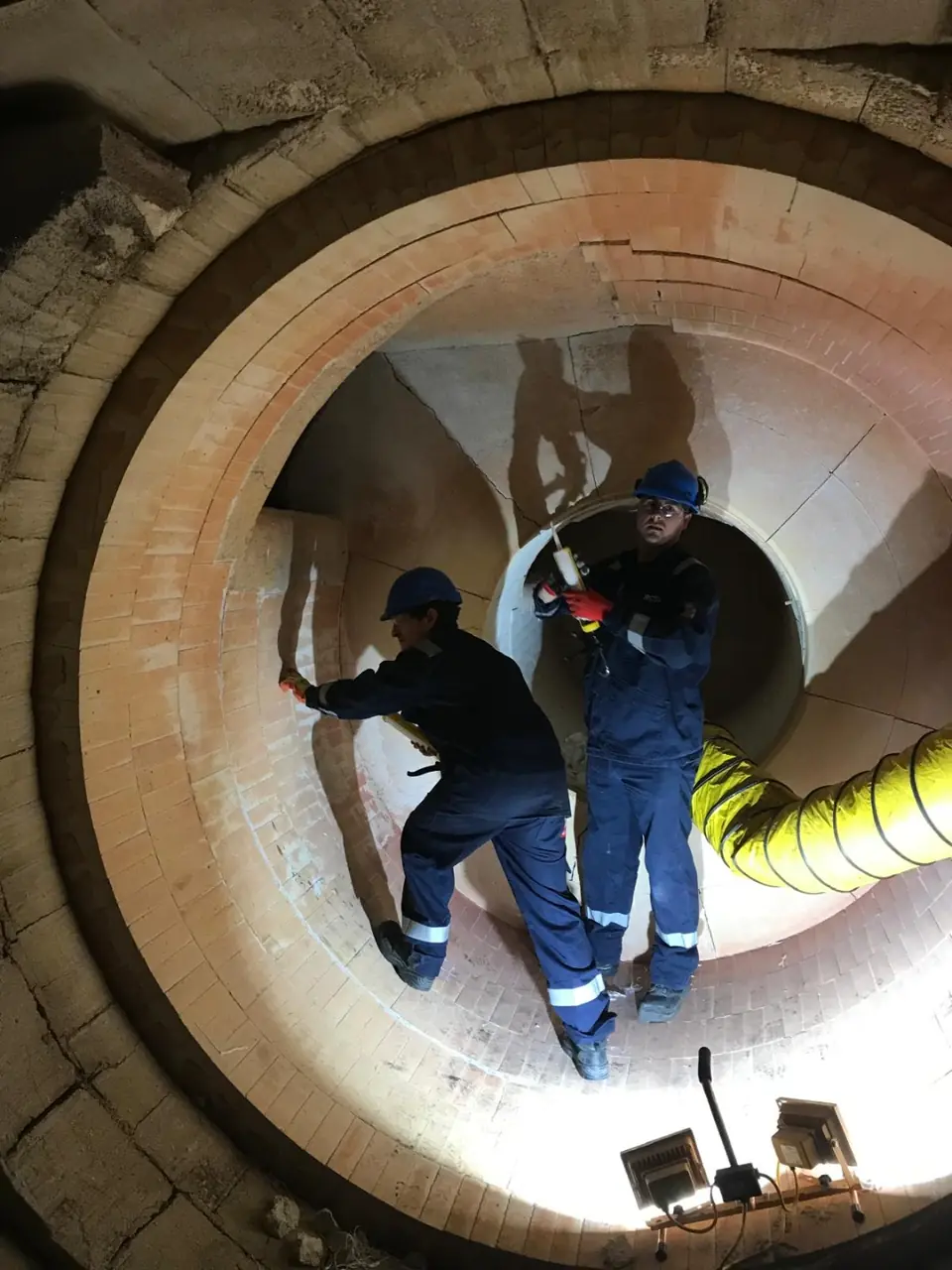 Two technicians working at the circular opening of refractory-lined equipment
